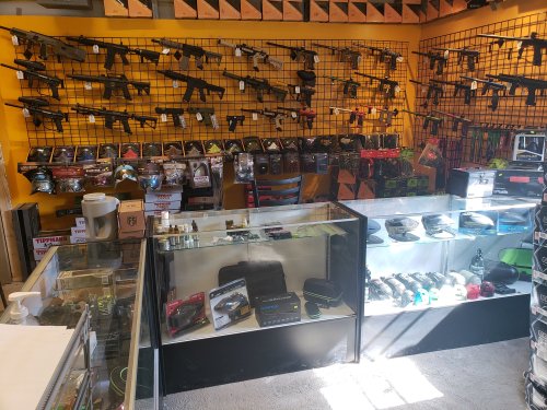 A display of airsoft guns and accessories in a brightly colored shop, with items arranged on shelves and in glass cases.