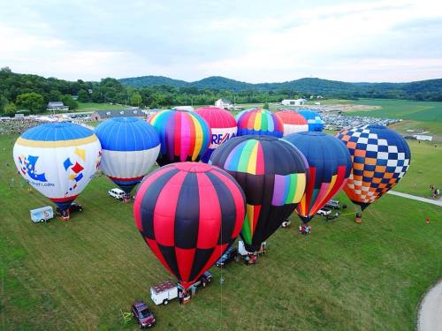 Aerial view of colorful hot air balloons on a grassy field with hills in the background.