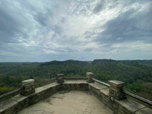 A stone overlook with a view of lush green hills under a cloudy sky.