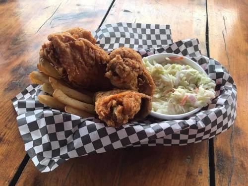 A basket of fried chicken, French fries, and coleslaw on a checkered paper, resting on a wooden table.