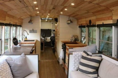Interior of a converted bus featuring wooden accents, cozy seating, and a kitchen area with modern appliances.