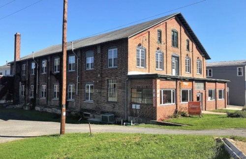 A brick building with multiple windows and a sign, set against a clear blue sky and green grass.