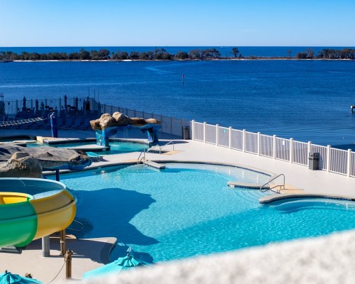 A sunny pool area with a water slide, overlooking a calm blue lake and clear sky.
