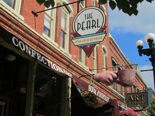 Signage for "The Pearl" ice cream parlor and "Confectionery" with a decorative cup, set against a brick building.