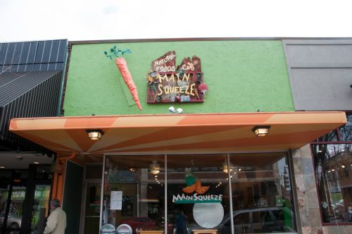A colorful storefront with a green wall and a sign reading "Main Squeeze" featuring a large carrot graphic.