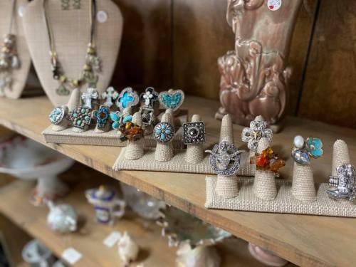 A display of various decorative rings on fabric-covered stands, set against a wooden background with other vintage items.