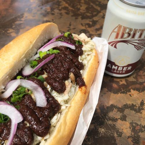 A sandwich filled with meat, topped with onions and green onions, next to a can of Abita Amber Lager.