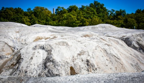 A landscape of white, sandy hills under a clear blue sky, surrounded by green trees in the background.