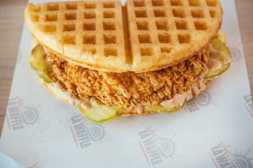 A crispy fried chicken sandwich with pickles, served between two golden waffles.