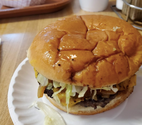 A close-up of a juicy burger with melted cheese, lettuce, and a shiny bun on a paper plate.