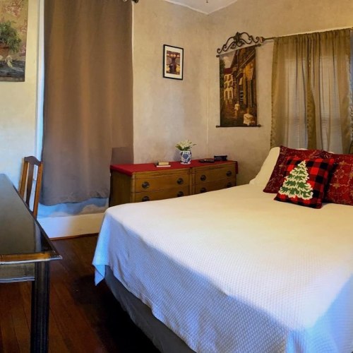 Cozy bedroom with a bed, wooden furniture, and decorative pillows, featuring warm tones and soft lighting.