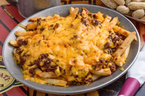 A plate of loaded fries topped with melted cheese and chili, served alongside a bowl of peanuts.