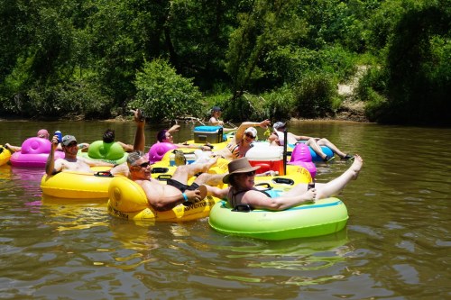 A group of people relaxes on colorful inner tubes while floating down a river on a sunny day.