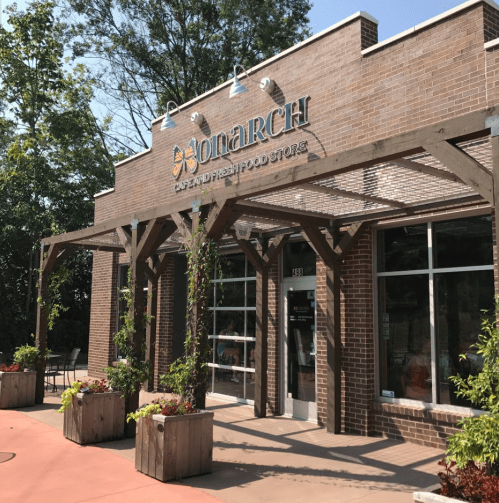 Exterior of a café and fresh food store named "Monarch," featuring a brick facade and outdoor seating area.