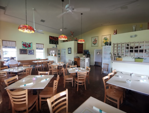 Brightly lit restaurant interior with wooden tables, chairs, and colorful pendant lights. A cozy, inviting atmosphere.