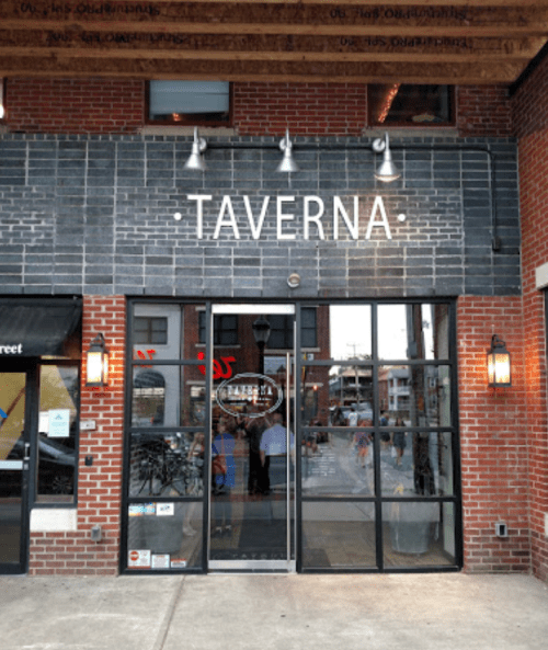 Exterior of a restaurant named "Taverna," featuring large glass doors and a brick facade.