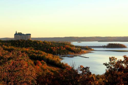 A scenic view of a lake surrounded by autumn foliage and a distant hotel against a sunset sky.