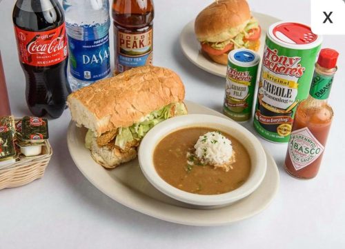 A plate with a sandwich, rice, and brown gravy, surrounded by drinks and condiments.