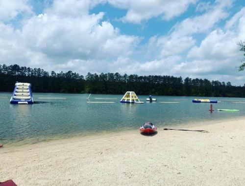 A sandy beach by a lake with inflatable water obstacles and a clear blue sky with scattered clouds.