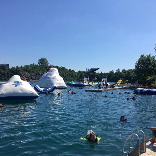 A sunny day at a water park with inflatable structures, people swimming, and trees in the background.