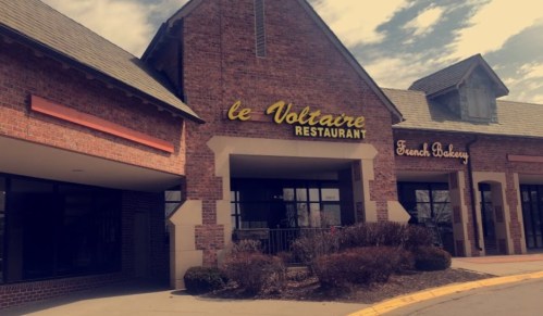 Exterior of a brick building featuring "le Voltaire Restaurant" and "French Bakery" signs.