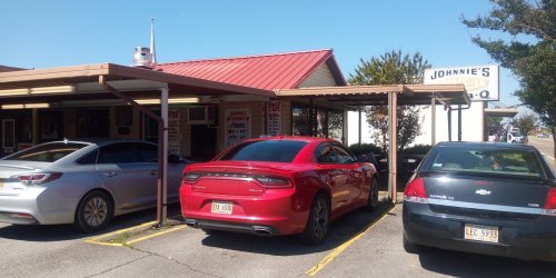 A red car parked outside Johnnie's BBQ restaurant, with two other cars and a clear blue sky in the background.