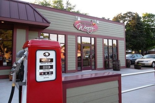 A vintage gas pump in front of a modern restaurant with a sign reading "Laws Station Winery." Cars parked nearby.