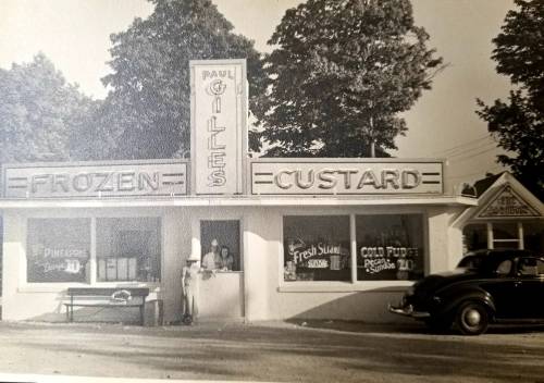 A vintage ice cream shop with a sign reading "Paul Gilles Frozen Custard," featuring a man behind the counter.