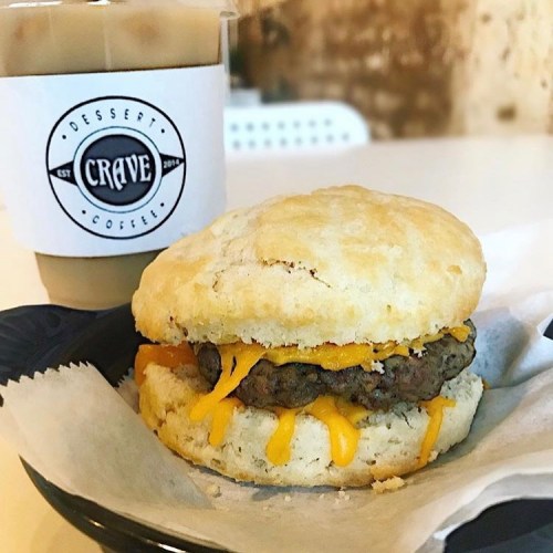 A biscuit sandwich with a beef patty and melted cheese, alongside a cup of iced coffee from Crave.