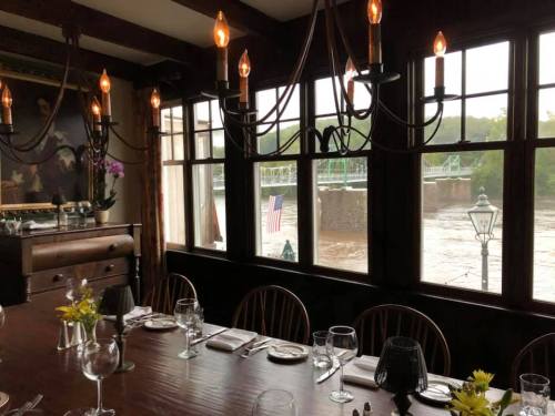A cozy dining room with a large table, chandeliers, and windows overlooking a river and a bridge.