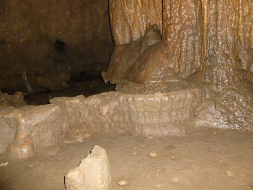 A dimly lit cave interior featuring textured rock formations and a small pool of water on the ground.