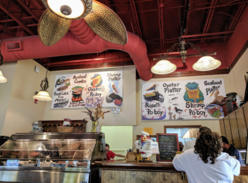 Interior of a seafood restaurant featuring a menu on the wall with various seafood dishes and a customer at the counter.