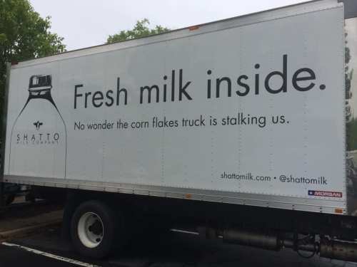 A truck from Shatto Milk Company with a humorous message about fresh milk and corn flakes.