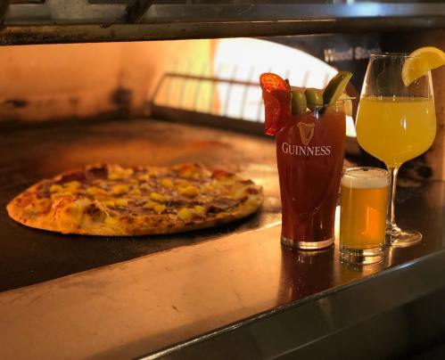 A pizza baking in an oven, accompanied by a Guinness glass, a cocktail with a lemon slice, and a small beer.