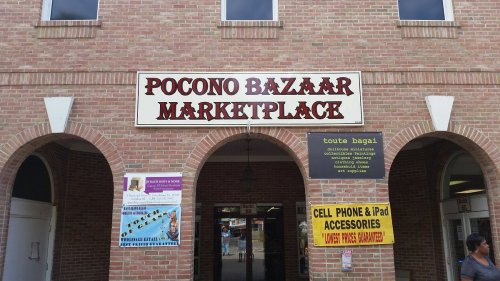 Entrance to Pocono Bazaar Marketplace, featuring various signs for shops and services in a brick building.