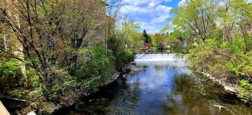 A serene river scene with lush greenery and a small waterfall under a blue sky with scattered clouds.