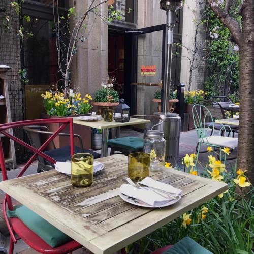 Outdoor dining area with colorful chairs, a wooden table, and blooming flowers in a cozy setting.