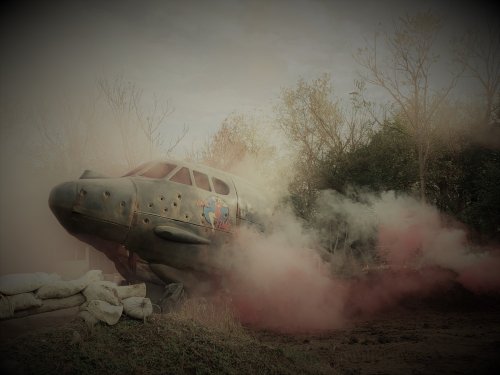 A vintage airplane surrounded by colorful smoke, set in a misty outdoor environment with trees in the background.