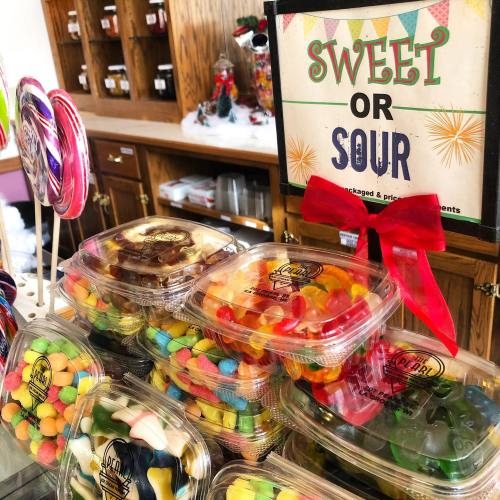 Colorful candy containers labeled "Sweet or Sour" with a festive sign and decorations in the background.