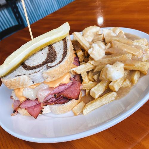 A hearty sandwich with layers of meat and cheese, served with fries topped with gravy and cheese curds.