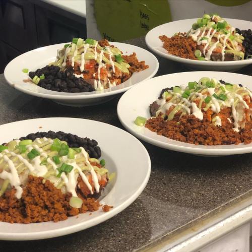 Four plates of colorful food featuring seasoned meat, black beans, and drizzled with sauce and green onions.
