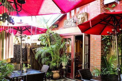 A cozy outdoor patio with red umbrellas, lush greenery, and rustic furniture, creating a warm, inviting atmosphere.