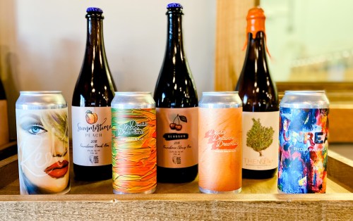 A wooden tray holds various craft beer bottles and cans with colorful labels, showcasing different flavors and designs.