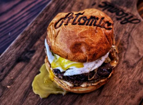 A gourmet burger with a fried egg, melted cheese, and a juicy patty, served on a wooden board.