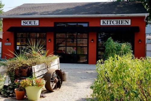 A vibrant red building with "Soul Kitchen" signs, surrounded by greenery and a rustic cart filled with plants.