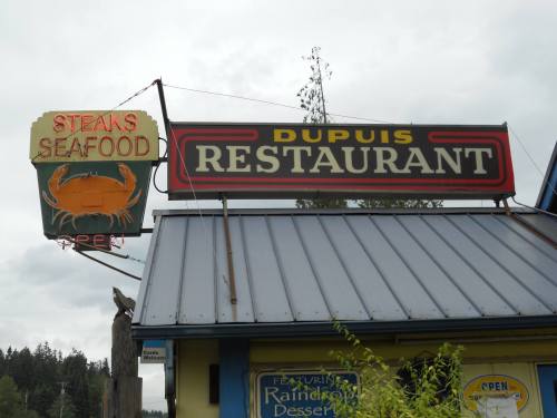 Sign for Dupuis Restaurant featuring "Steaks Seafood" and an open symbol, set against a cloudy sky.