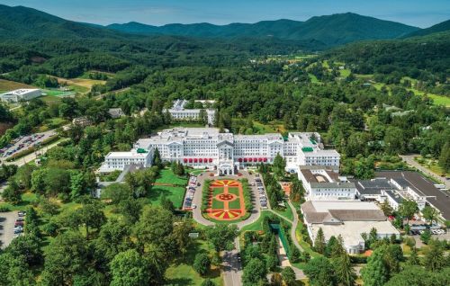 Aerial view of a large hotel surrounded by lush greenery and mountains, featuring landscaped gardens in the foreground.