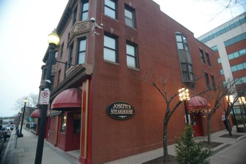 Exterior of Joseph's Steakhouse, a brick building with red awnings, street lamps, and nearby trees.