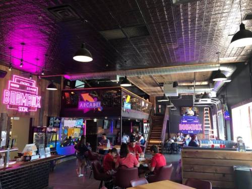 A vibrant arcade and dining space with neon signs, seating areas, and a lively atmosphere.