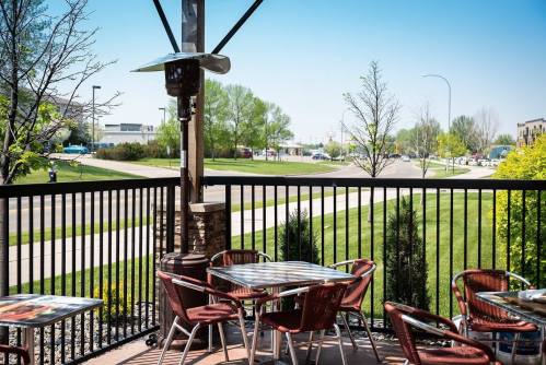 Outdoor dining area with tables and chairs, surrounded by greenery and a clear blue sky.